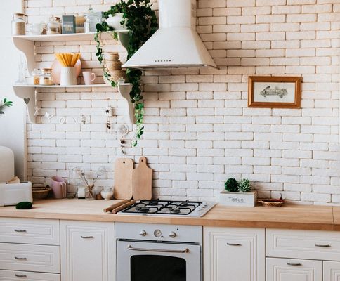 Ein Ausschnitt aus einer hellen Küche mit einer weißen Steinwand, vielen Gegenständen aus Naturmaterialien wie Holz und einer Pflanze