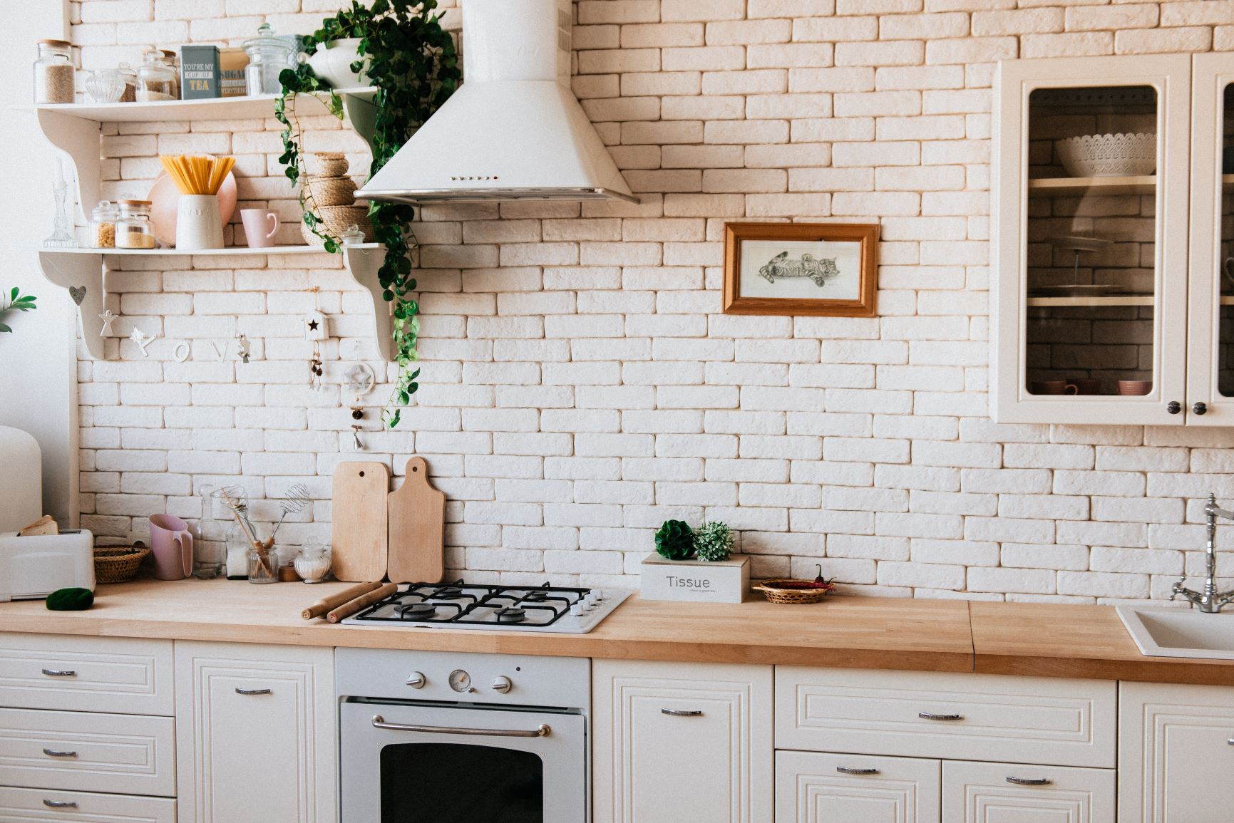 Ein Ausschnitt aus einer hellen Küche mit einer weißen Steinwand, vielen Gegenständen aus Naturmaterialien wie Holz und einer Pflanze