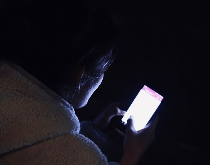 Mensch am Handy im Dunkeln, das Handylicht leuchtet