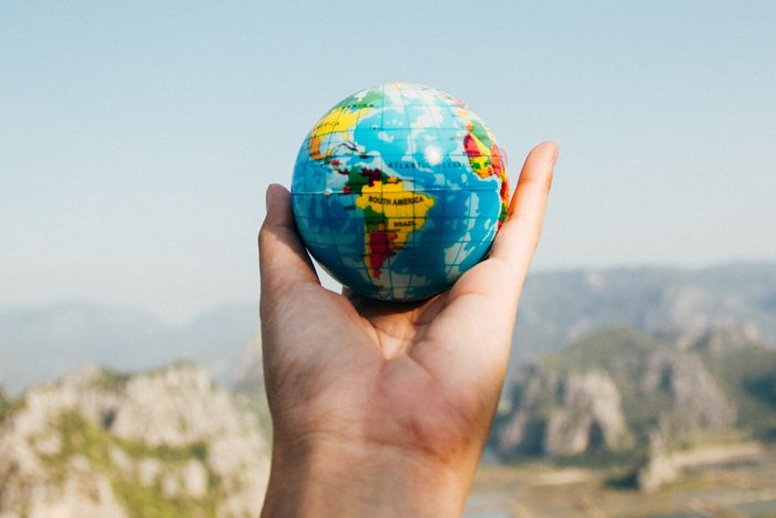 Ein Globus wird geschützt in einer Hand gehalten, im Hintergrunf eine bergige Landschaft