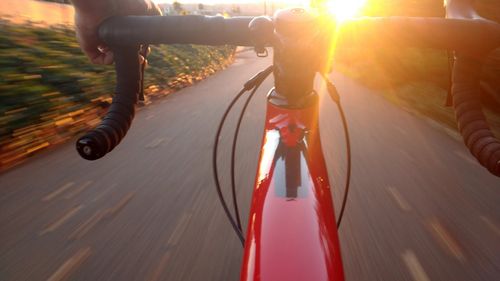 Fahrradlenker im Vordergrund mit Blick auf die Straße mit Sonnenuntergang im Hintergrund.