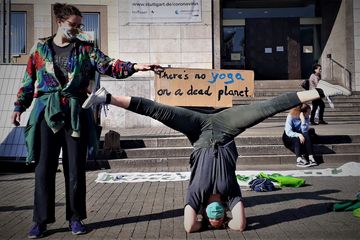 Eine junge Frau macht eine Yoga-Übung und eine andere Frau hält das Demo-Schild mit der Aufschrift: There´s no yoga on a dead planet