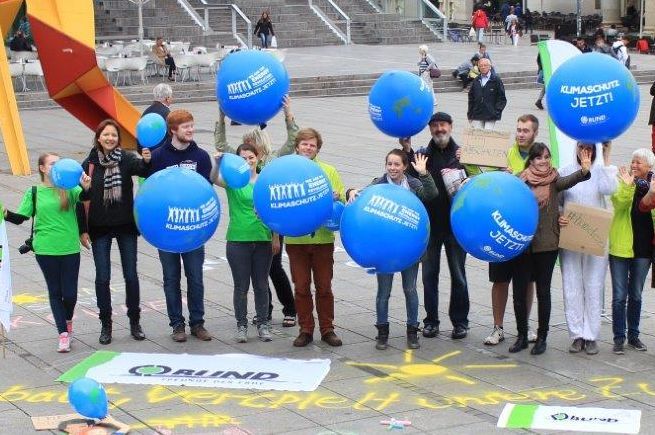 Kreide-Aktion auf dem Stuttgarter Schlossplatz. Menschen halten Luftballons mit dem Aufdruck "Klimaschutz Jetzt". 