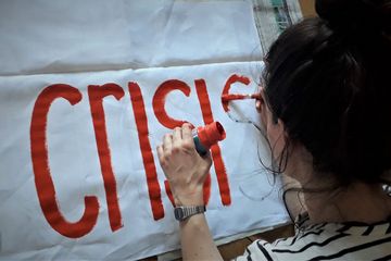 Eine junge Frau mal ein Banner, zu sehen ist das englische Wort "Crisis"