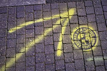 EIn Pfeil und das FFF-Logo sind mit gelber Kreide auf die Straße geschrieben