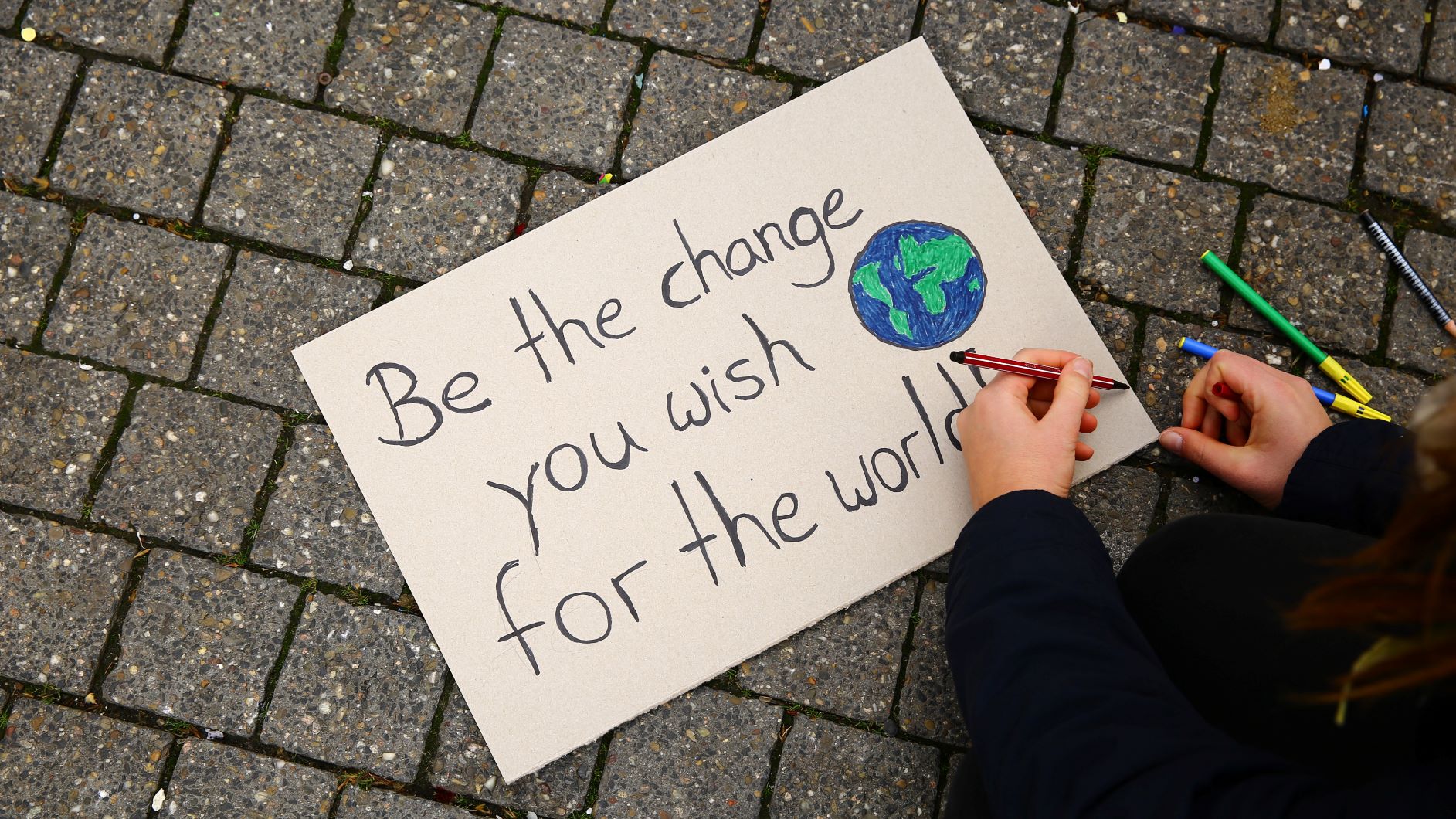 Eine Person malt ein Demo-Schild mit dem Spruch "Be the change you wish for the world"