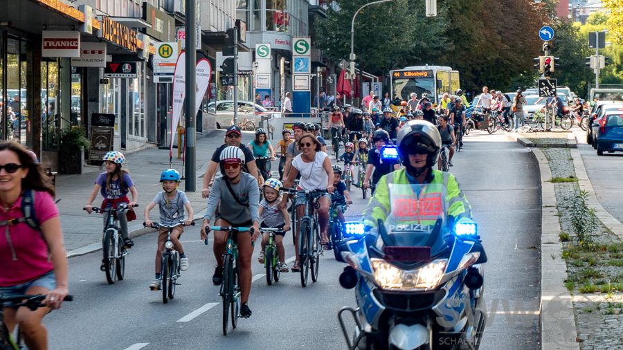 Viele Kinder auf Fahrrädern fahren auf der Straße begleiet von Eltern und einem Polizei-Motorrad