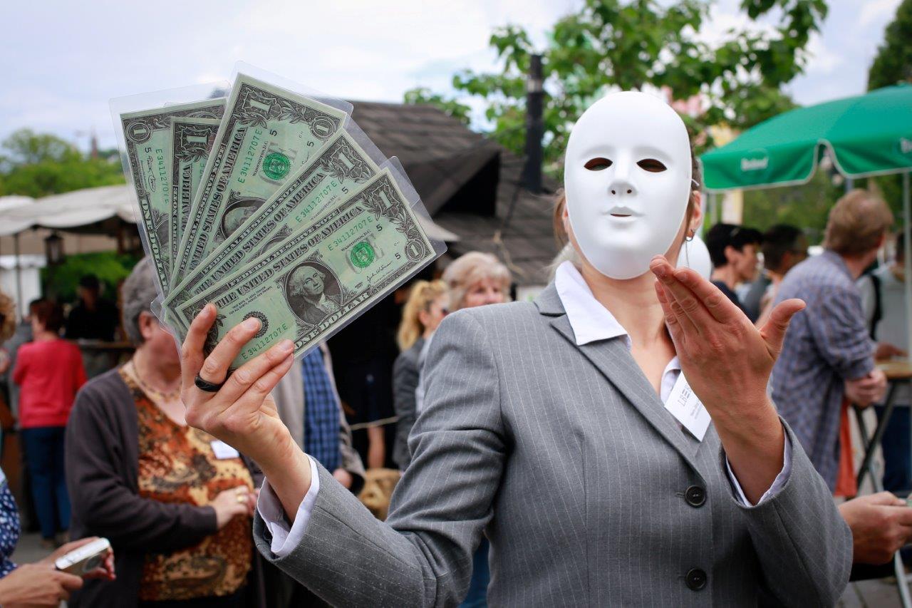 Person mit weißer Maske hält Geldscheine in die Luft. 